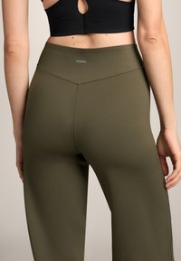 Olivově zelené legíny s vysokým pasem, s hladkou, elastickou texturou a decentním logem OYSHO na zadní straně. Jednoduchý, elegantní design.