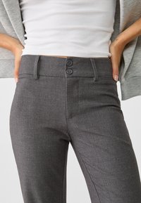 Pantalons taillés gris avec une texture lisse, coupe slim et fermeture à bouton double à la taille ; comprend des poches latérales et des lignes épurées.
