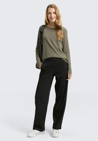 Olijfkleurige top met lange mouwen gecombineerd met zwarte geplooide, getailleerde broek en witte sneakers. De outfit heeft een ontspannen pasvorm en een eenvoudig ontwerp.