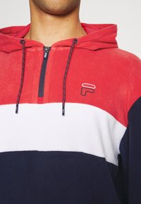Sweat à capuche rayé rouge, blanc et marine avec une fermeture éclair quart et des détails de logo. Fabriqué en polaire douce avec une finition texturée.