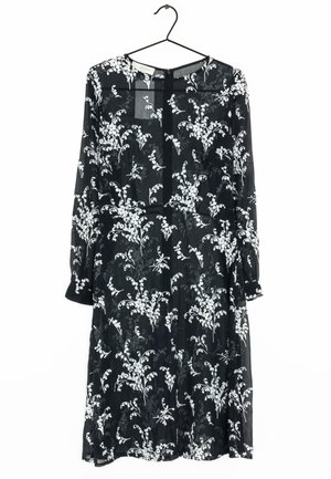Robe noire en tissu transparent ornée de motifs floraux blancs. Manches longues, encolure ronde et fermeture à boutons au dos.