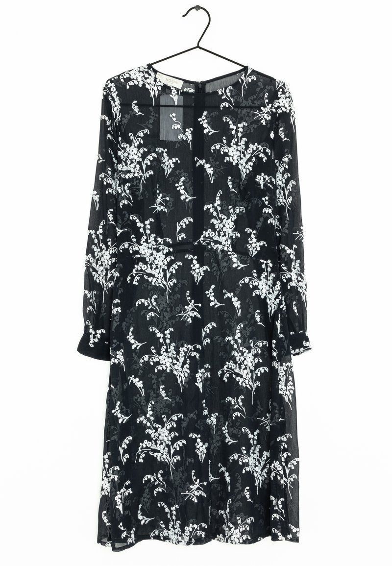Musta mekko, joka on valmistettu läpinäkyvästä kankaasta ja jossa on valkoisia kukkakuoseja. Pitkät hihat, pyöreä pääntie ja takana nappikiinnitys.