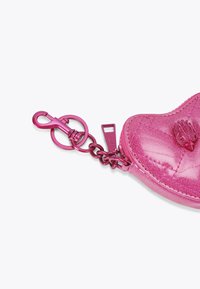 Borsetta in pelle lucida e rosa a forma di cuore, con superficie testurizzata e accessori metallici, tra cui un gancio a moschettone e una catena.