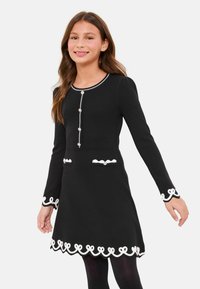 Rochie neagră cu mâneci lungi, cu bordură albă, tivuri dințișoare și nasturi decorativi. Două buzunare frontale cu detalii asortate.