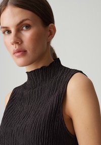 Black sleeveless top with a high, ruffled collar. Textured fabric features a wavy pattern, highlighting a fitted silhouette.