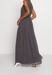 Lång grå aftonklänning med en figursydd pärlbesatt överdel och en flödande chiffongkjol. Matcher med vita högklackade skor.