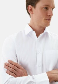 Witte button-up overhemd met een klassieke kraag, lange mouwen en een borstzak; gladde textuur en een aansluitend ontwerp.