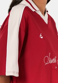 Rode polo met witte schouderaccenten en kraag, met geborduurde details. Gemaakt van een gladde stof, met een ontspannen pasvorm.
