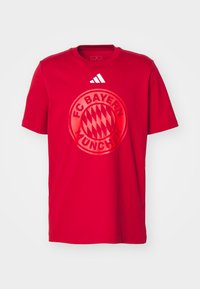 Red cotton t-shirt featuring a large circular FC Bayern München logo in the center. Adidas three-stripe logo on the upper right.