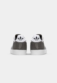 Grå mockasinsneakers med vita gummisulor, med tre svarta ränder och en logotyp baktill. Låg profil med vadderad krage.