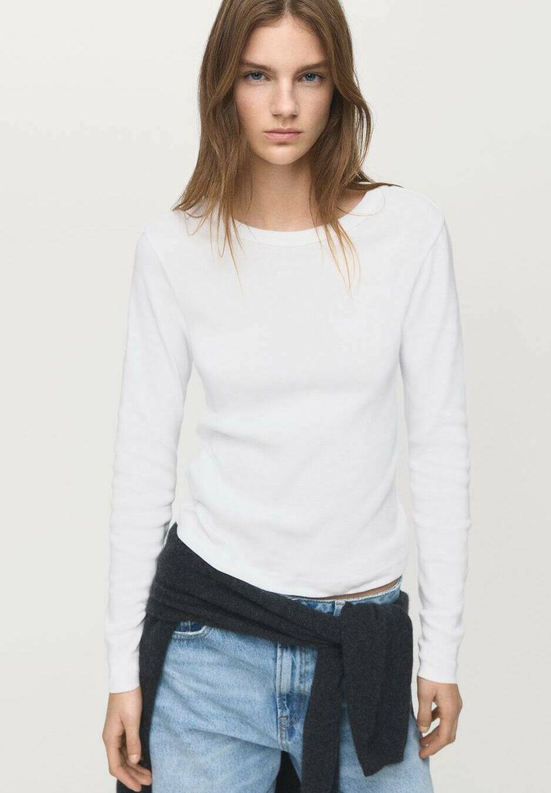 Cămașă albă cu mâneci lungi din bumbac, asociată cu blugi albaștri. Un pulover gri închis este legat în jurul taliei. Design simplu, ajustat.