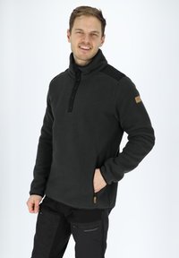 Pullover in pile grigio scuro con colletto alto, accenti neri sulle spalle, chiusura anteriore con bottoni e cerniere laterali per tasche.