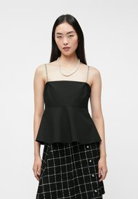 Czarny top peplum z cienkimi, błyszczącymi ramiączkami. Posiada usztywniony gorset i rozkloszowany dół. Model zestawia go z czarno-białą spódnicą w kratę.