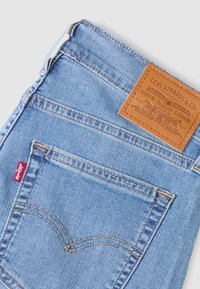 Ανοιχτό μπλε τζιν παντελόνι με δερμάτινο μπαλώμα που φέρει ανάγλυφο λογότυπο, ορατή ραφή και μια μικρή κόκκινη ετικέτα Levi's στην πίσω τσέπη.