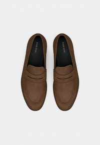 Καφέ σουέτ μοκασίνια με σχεδιασμό slip-on, ραμμένες λεπτομέρειες και υφασμένο επάνω μέρος. Το εσωτερικό διαθέτει μαύρη επένδυση με το όνομα της μάρκας.