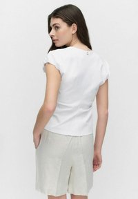 Witte top met korte mouwen en geplooide mouwdetails, met een knoopsluiting op de achterzijde. Gecombineerd met lichtbeige linnen shorts.