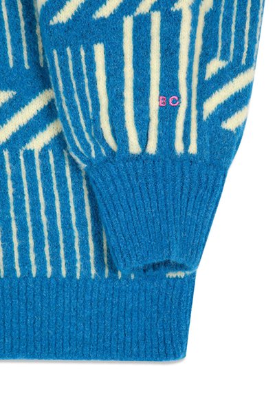 Manche de pull en laine à motif bleu et blanc avec poignet côtelé et petites lettres brodées roses "BC" près du poignet.