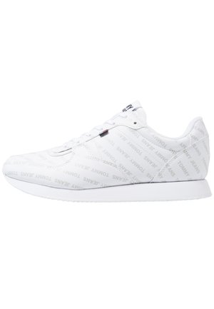 Sneaker bianca bassa con motivo testuale "Tommy Jeans", suola bianca e piccolo etichetta con bandiera rossa, bianca e blu sul lato.