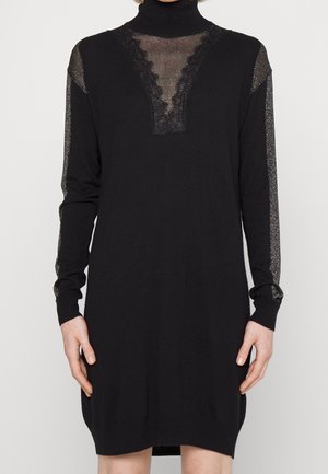 Robe noire à col roulé, avec des panneaux accentués transparents et scintillants ainsi qu'une bordure en dentelle au niveau de l'encolure. Manches longues et coupe décontractée.
