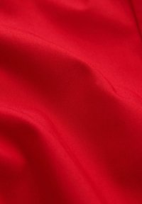 Glatter roter Stoff mit sanften Falten und weicher Textur, der Lichtreflexionen auf der Oberfläche zeigt.
