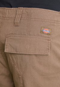 Hnedé pracovné nohavice s textúrovaným povrchom, s jednou zadnou vreckom a prešitou nášivkou s logom Dickies.