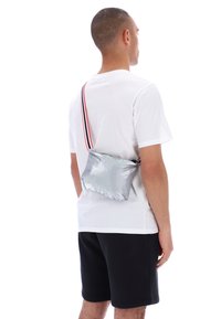 Hombre con camiseta blanca y pantalones cortos negros lleva una pequeña bolsa cruzada plateada con una correa a rayas en la espalda.