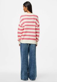 Pull en tricot rayé rose et blanc avec des découpes, associé à un pantalon en denim bleu à jambes larges. Le pull a un col et des poignets côtelés.