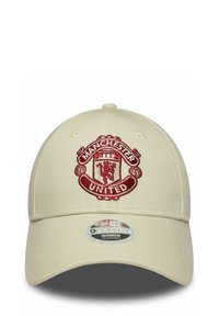 Beige Kappe mit einem gebogenen Schirm, die auf der Vorderseite mit einem roten, gestickten Manchester United-Logo versehen ist und einen verstellbaren Rücken hat.