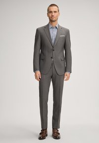 Gray suit with a notched lapel, two buttons, and side pockets. Underneath, a blue patterned shirt is visible. Brown leather shoes complete the look.