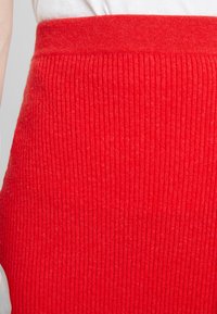 Rode geribde gebreide rok met een aansluitende tailleband. De textuur is zacht en rekbaar, met een consistent patroon over de gehele rok.