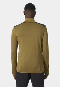 Długi rękaw sweter w oliwkowym kolorze z kołnierzem na zamek, z niebieskimi panelami na ramionach i teksturowanym materiałem. Zawiera otwory na kciuki w mankietach.