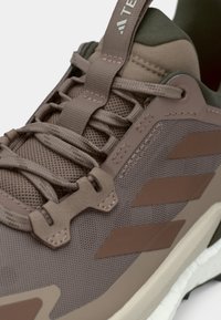 Pruunide ja roheliste toonidega sportjalanõud, millel on tekstuuriga võrgus ülaosa, lamedad paelad ja kolm pruuni triipu külgedel; varustatud pehmendusega tallaga.