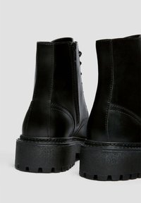 Czarne skórzane buty za kostkę mają solidną gumową podeszwę, sznurowane z przodu oraz zamek błyskawiczny z boku, charakteryzują się gładką teksturą i wzmocnionymi detalami szycia.