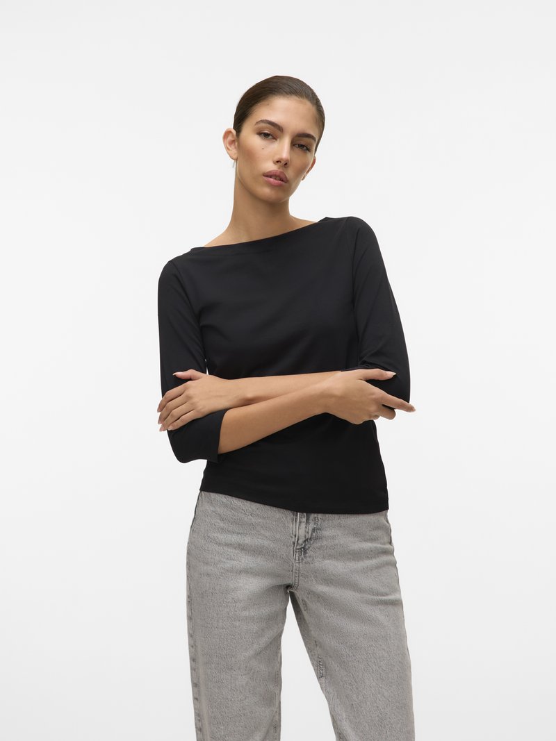 Svart langermet topp med båtutskjæring, kombinert med høyt liv lysegrå jeans med en falmet tekstur og avslappet passform.