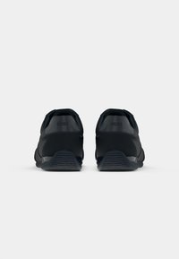 Black athletic shoes with a smooth textile upper, rubber sole, and embossed logo on the heel, featuring a sleek and modern design.