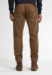 Bruine corduroybroek met geribbelde textuur, voorzien van twee achterzakken en gestyled met bruine enkellaarzen.
