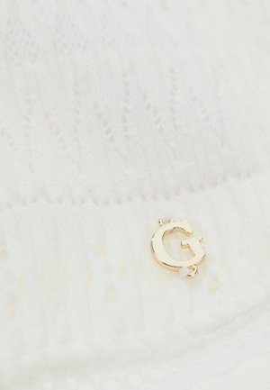 Weißes Strickgewebe mit einem kleinen goldfarbenen Metallbuchstaben "G", der nahe dem unteren Rand befestigt ist.