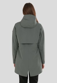 Trench verde resistente all'acqua con cappuccio, dotato di vita sagomata, spacco posteriore e texture liscia. Dettagli chiave includono maniche lunghe e lunghezza fino a metà coscia.
