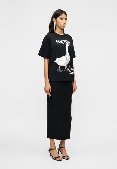 Μαύρο υπερμέγεθες μπλουζάκι με εικόνα λευκής πάπιας με κόκκινο ράμφος και παπούτσια, συνδυασμένο με μακριά μαύρη φούστα και μαύρα πέδιλα με λουράκια.