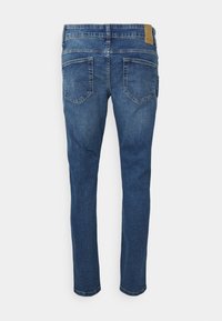 Jeans skinny em denim azul escuro. Apresenta uma cintura com um patch de couro bege e dois bolsos traseiros com um ligeiro detalhe em costura.