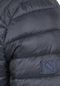 Marine pufferjack met doorgestikte naden en een rechthoekig stoffen label. Glad, glanzend materiaal met een geïsoleerd ontwerp voor warmte.