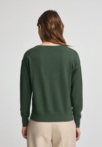 Un pull en tricot vert avec des manches longues, une coupe décontractée et un col large. Texture lisse et détail de bord côtelé.