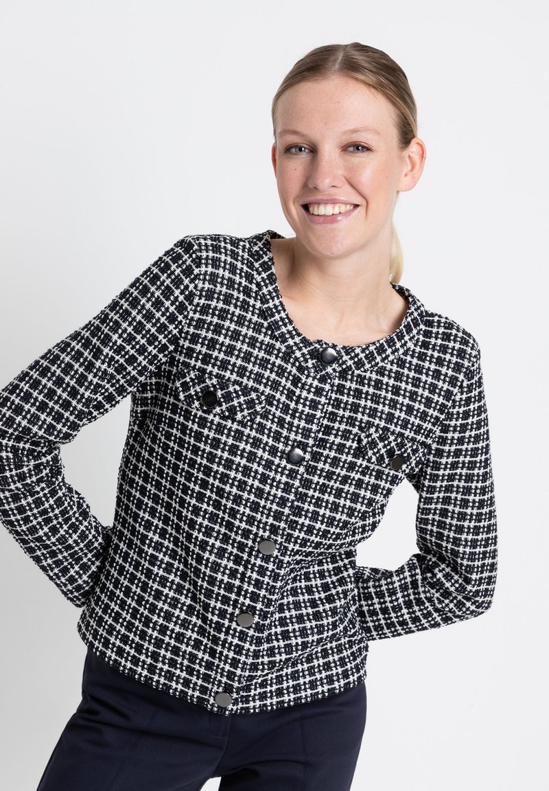 Tweedjacke in Schwarz und Weiß mit Rundhalsausschnitt, zwei Brusttaschen mit Klappen und schwarzen Knöpfen entlang der Vorderseite.
