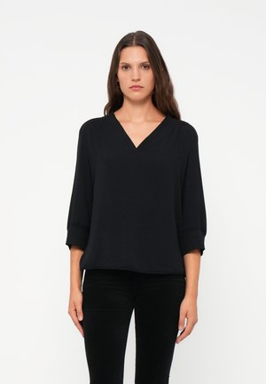 Zwarte V-hals blouse met driekwart mouwen, losse pasvorm, zachte textuur en een rechte zoom. Gecombineerd met aansluitende zwarte broeken.