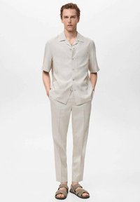 Light beige short-sleeve shirt with a collar, button front, and front pocket; matching tapered trousers; gray sandals. Smooth fabric texture.