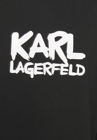 Camiseta negra con un gran texto blanco que dice "KARL LAGERFELD" en una expresión de fuente de pincel.