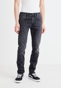 Jeans de mezclilla gris con corte slim, que cuentan con bolsillos frontales, cierre de botón y un ligero desgaste. Combinados con zapatillas en blanco y negro.
