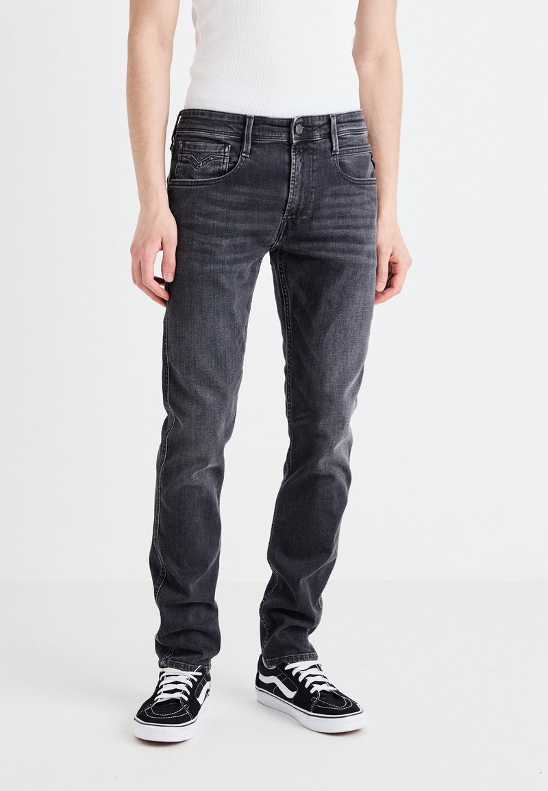 Jeans de mezclilla gris con corte slim, que cuentan con bolsillos frontales, cierre de botón y un ligero desgaste. Combinados con zapatillas en blanco y negro.