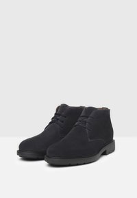 Stivali alla caviglia in suede blu scuro con una texture liscia, design con lacci, punta rotonda e suola in gomma nera. Adatti per un look casual.