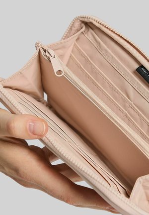 Portafoglio beige aperto che mostra molteplici fessure per carte, una tasca centrale con cerniera e un interno spazioso su uno sfondo neutro.